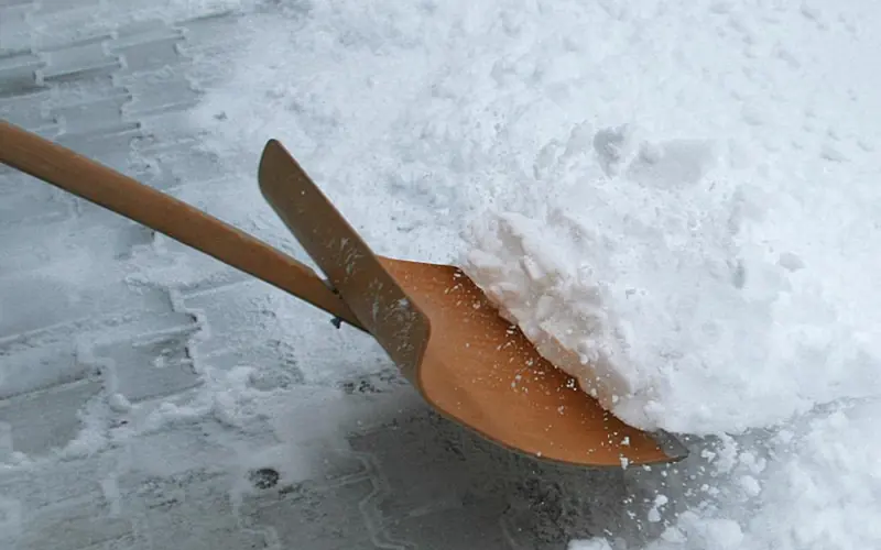 Schneeschaufel räumt frischen Schnee von einem Gehweg